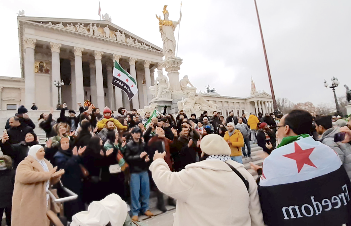 Figure 2. At the same demonstration, a group of people sings revolutionary songs and shout slogans against the backdrop of the Austrian parliament and the statue of Athena (still from a video recorded by the author, see Christidis 2025).