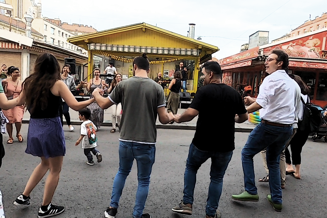 Figure 7. Vienna, June 22, 2023. Concert of the band Dabke-Dilan in the outdoor area in front of the social and intercultural space called Stand 129, near Viktor-Adler-Markt in Favoriten (10th district). Salah Ammo (right) has left the stage to join the circular dance unfolding in the middle of the street (photo by the author).
