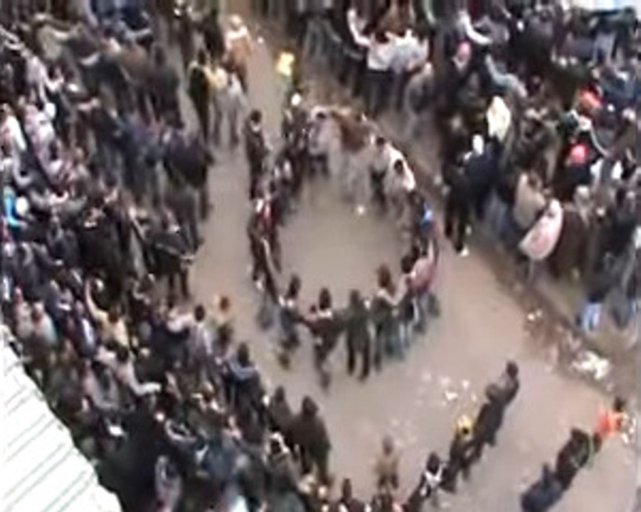 Figure 3. Stills from the YouTube video “Homs, Syria, 30 December 2011: The Khalidiya sit-in on the ‘Friday of the march to the squares,’ with Abdul Baset Al-Sarout, and ‘Paradise, oh our homeland’” uploaded by AhfadKhaled (2011a). The still image on the left (2:47) shows a dance circle formed inde-pendently within the assembled crowd. The still image on the right (2:58) shows the entire crowd forming concentric circles, swaying left and right to the rhythm of the song, surrounding the replica of the Homs Clock Tower (stills created by the author).