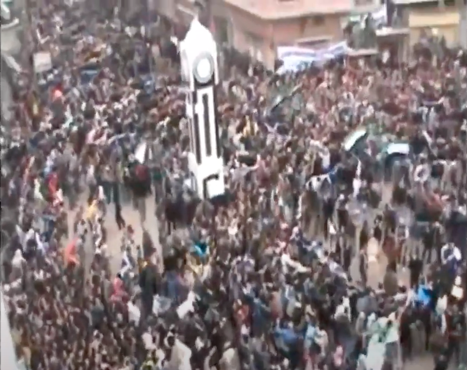 Figure 3. Stills from the YouTube video “Homs, Syria, 30 December 2011: The Khalidiya sit-in on the ‘Friday of the march to the squares,’ with Abdul Baset Al-Sarout, and ‘Paradise, oh our homeland’” uploaded by AhfadKhaled (2011a). The still image on the left (2:47) shows a dance circle formed inde-pendently within the assembled crowd. The still image on the right (2:58) shows the entire crowd forming concentric circles, swaying left and right to the rhythm of the song, surrounding the replica of the Homs Clock Tower (stills created by the author).